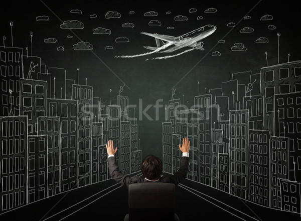 Stock photo: Businessman sitting in front of a cityscape drawing on a chalkbo