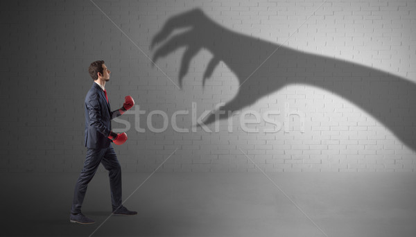 Businessman fighting with scary hand shadow Stock photo © ra2studio
