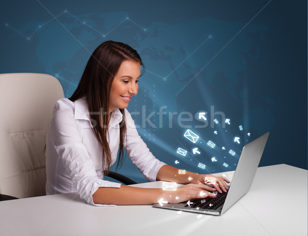 Young lady sitting at dest and typing on laptop with message ico Stock photo © ra2studio