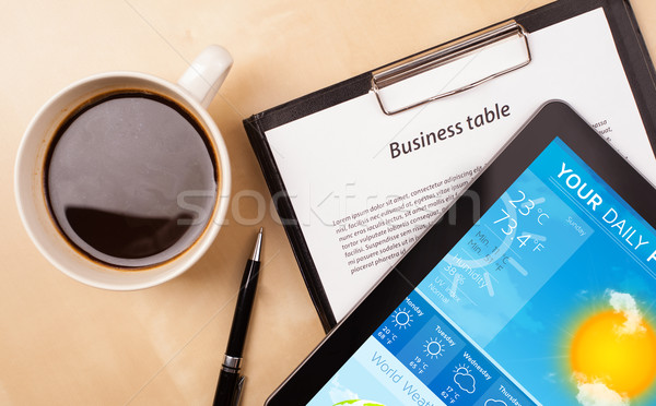 Stock photo: Workplace with tablet pc showing weather forecast and a cup of coffee on a wooden work table closeup