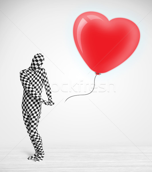 Cute guy in morpsuit body suit looking at a red balloon shaped heart Stock photo © ra2studio