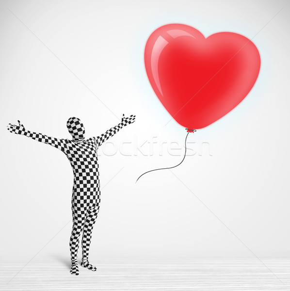 Cute guy in morpsuit body suit looking at a red balloon shaped heart Stock photo © ra2studio