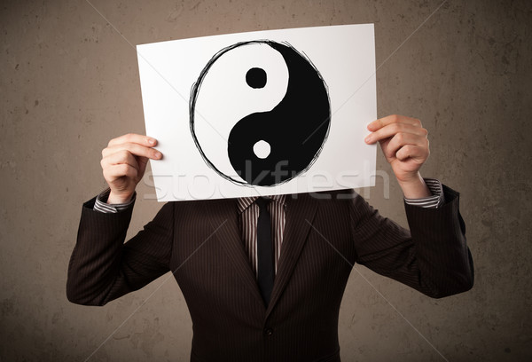 Businessman holding a paper with a yin-yang on it in front of hi Stock photo © ra2studio