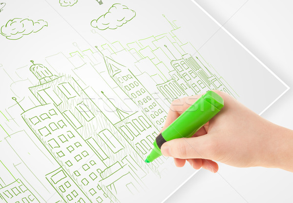 Stock photo: A person drawing sketch of a city with balloons and clouds on a plain paper
