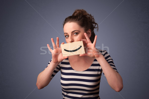 Happy pretty woman holding card with funny smiley Stock photo © ra2studio
