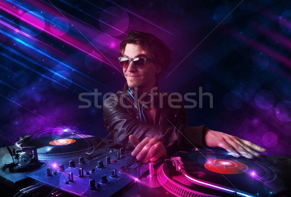 Stock photo: Young DJ playing on turntables with color light effects