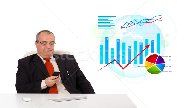 Businessman sitting at desk with statistics and holding a mobilephone, isolated on white Stock photo © ra2studio