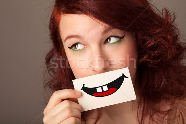 Happy pretty woman holding card with funny smiley Stock photo © ra2studio