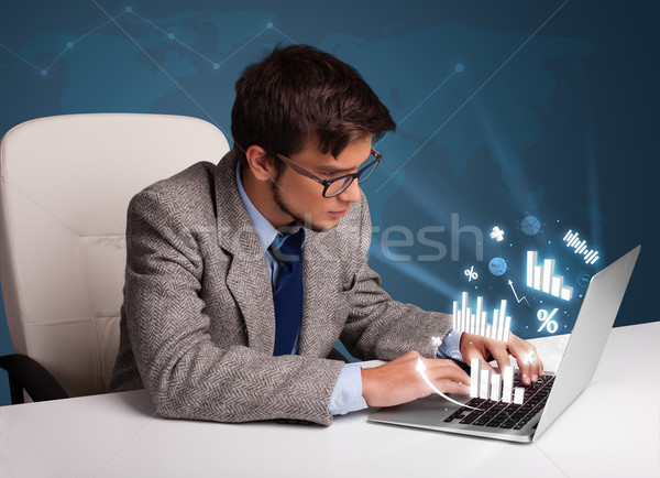 Young man sitting at desk and typing on laptop with diagrams and graphs comming out Stock photo © ra2studio