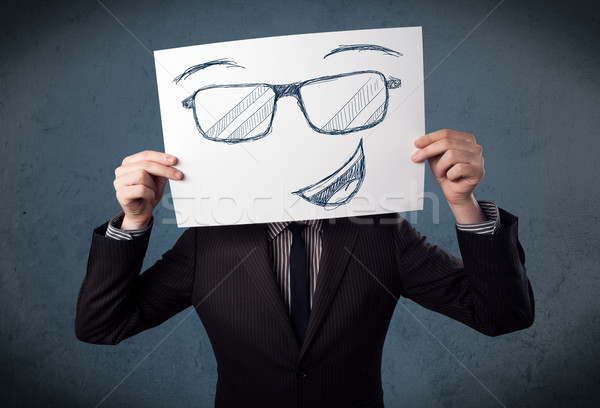 Businessman holding a paper with smiley face in front of his hea Stock photo © ra2studio