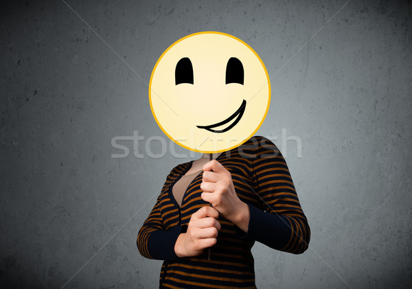 Young woman holding a smiley face emoticon Stock photo © ra2studio