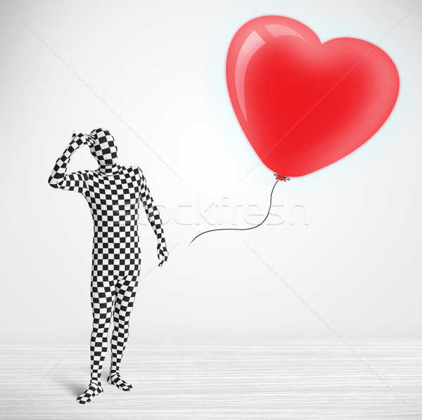 Cute guy in morpsuit body suit looking at a red balloon shaped heart Stock photo © ra2studio