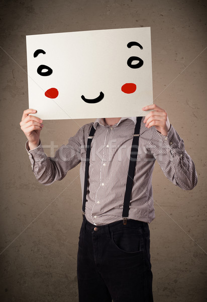 Stock photo: Businessman holding a cardboard with a smiley face on it