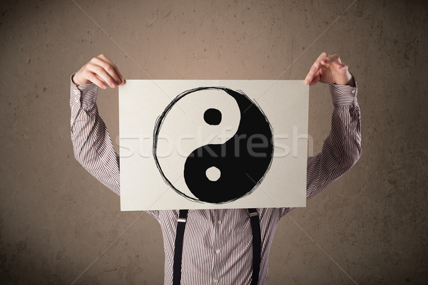 Businessman holding a paper with a yin-yang on it in front of hi Stock photo © ra2studio