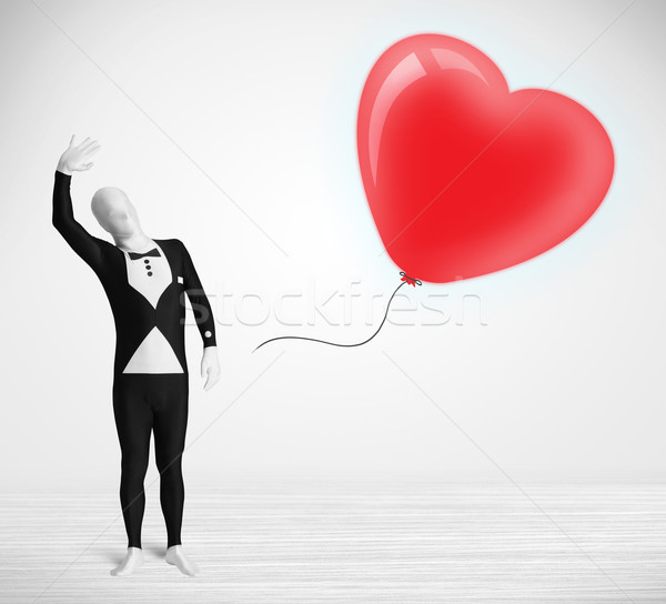 Cute guy in morpsuit body suit looking at a red balloon shaped heart Stock photo © ra2studio