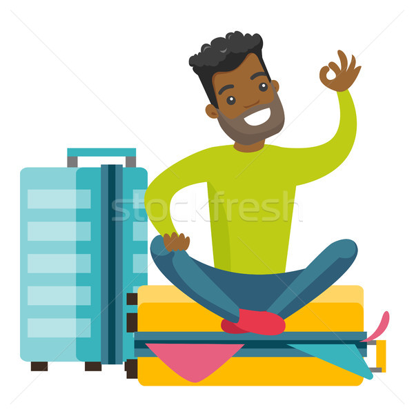 Young african-american man sitting on suitcase. Stock photo © RAStudio