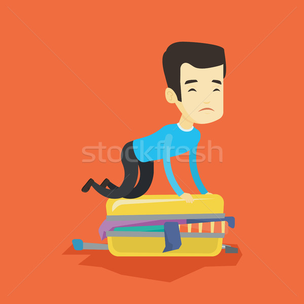 Stock photo: Young man trying to close suitcase.