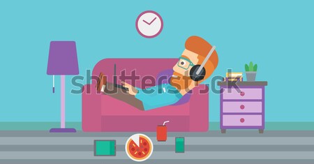 Stock photo: Man lying on sofa with many gadgets.