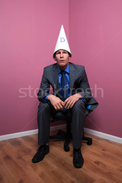 Businessman sat in corner wearing dunce hat Stock photo © RTimages