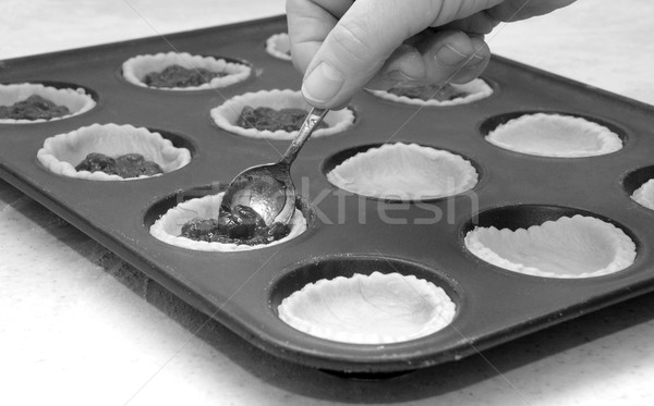 Stock photo: A woman's hand holding a teaspoon as she fills jam tarts