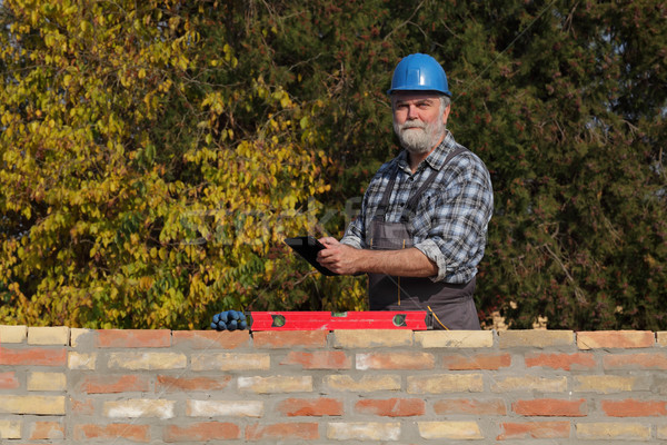 Worker examining brick wall, using tablet Stock photo © simazoran