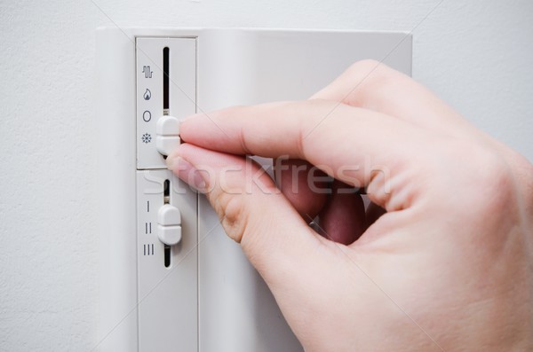 Hand switches air conditioner thermostat on wall Stock photo © simpson33