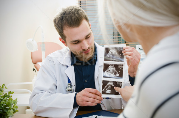 Stock photo: Doctor showing baby ultrasound image to pregnant woman.