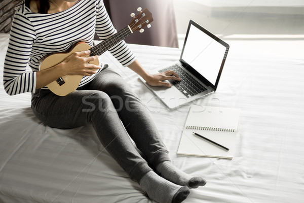 Happy young asian woman playing ukulele sitting on bed in bedroo Stock photo © snowing