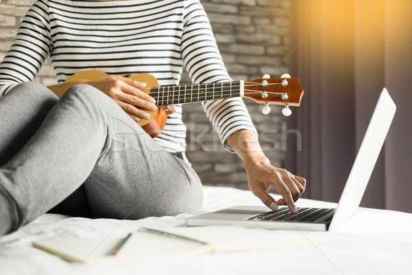 Happy young asian woman playing ukulele sitting on bed in bedroo Stock photo © snowing