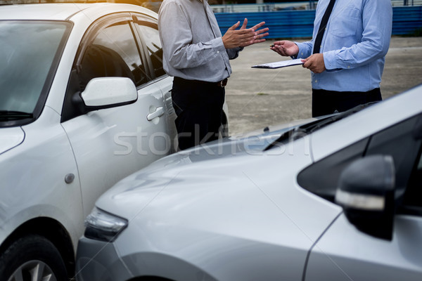 Insurance agent writing on clipboard while examining car after a Stock photo © snowing