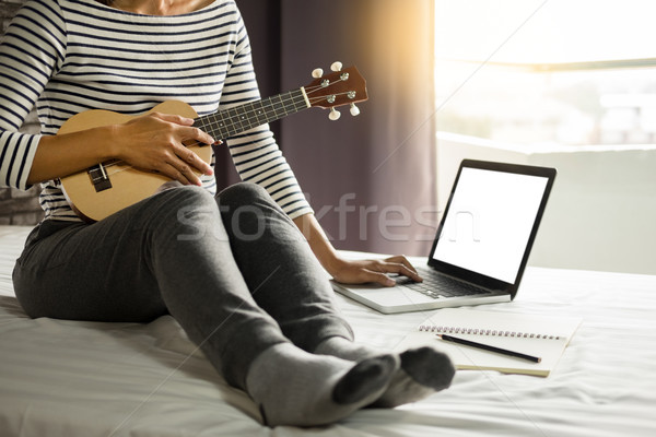 Happy young asian woman playing ukulele sitting on bed in bedroo Stock photo © snowing