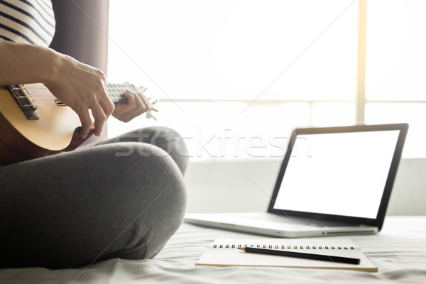 Happy young asian woman playing ukulele sitting on bed in bedroo Stock photo © snowing