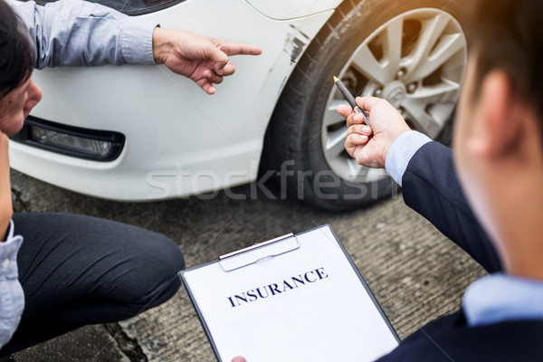 Insurance agent writing on clipboard while examining car after a Stock photo © snowing