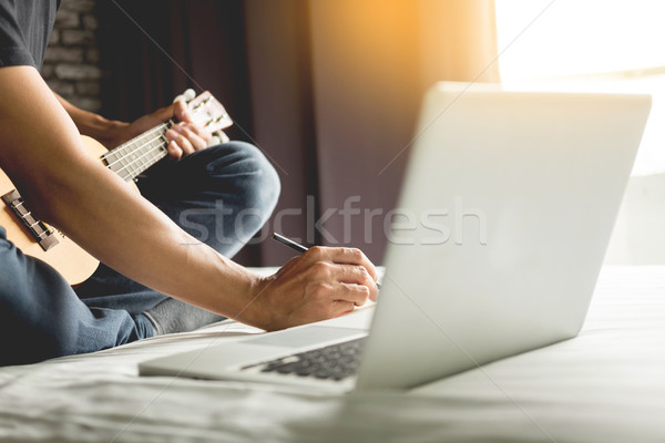 Happy young asian man playing ukulele sitting on bed in bedroom. Stock photo © snowing