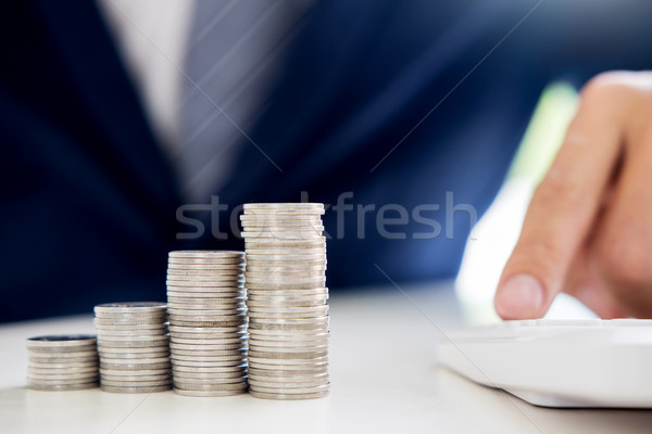 Business man putting coin to rising pile of money and calculator Stock photo © snowing