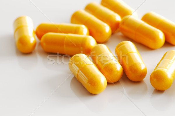 Stock photo: A handful of turmeric capsules on white reflective ceramic surface