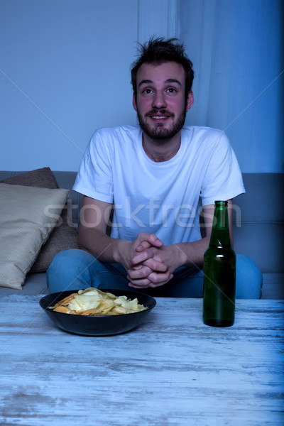 Young man watching TV at nighttime with chips and beer Stock photo © Spectral