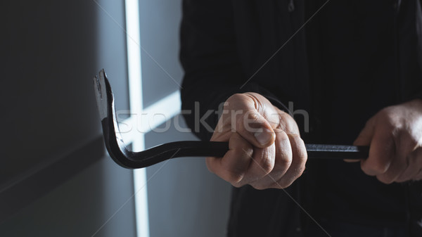 Stock photo: Burglar using a crowbar to break into a house
