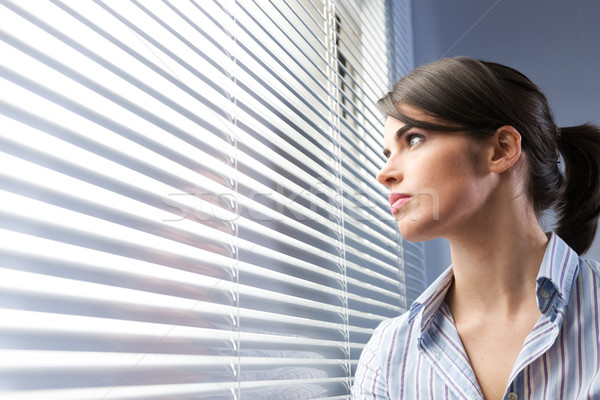Stock photo: Attractive woman peeking through blinds
