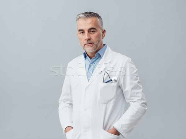 Orvos pózol visel laborköpeny néz kamera Stock fotó © stokkete