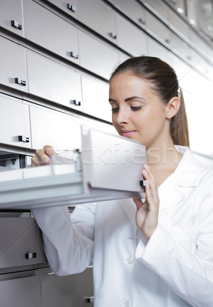 Stock photo: Young female pharmacist reaching for medicine