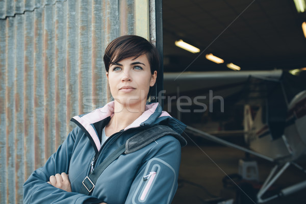 Stock photo: Smiling woman leaning against the hangar walls