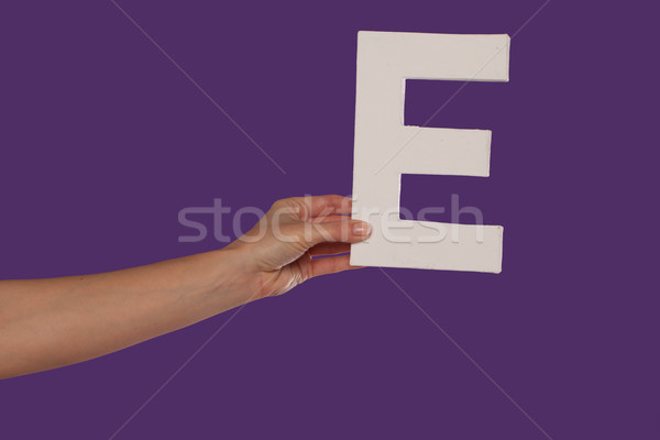 Stock photo: Female hand holding up the letter E from the left