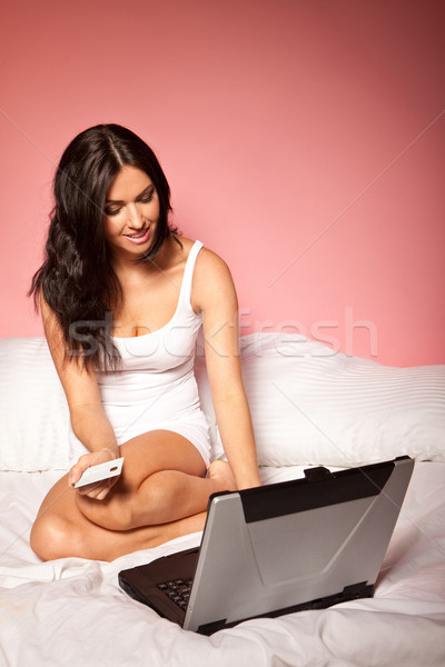 Shopping online pretty woman rannicchiata letto utilizzando il computer portatile Foto d'archivio © stryjek