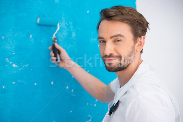 Attractive bearded young painter in dungarees standing looking at the camera holding up a roller Stock photo © stryjek