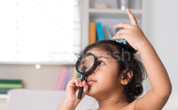 Indian girl peeking through magnifying glass. Stock photo © szefei