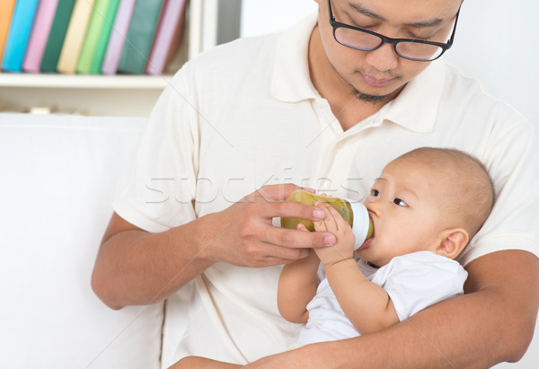 Stock photo: Father bottle feeding baby at home.