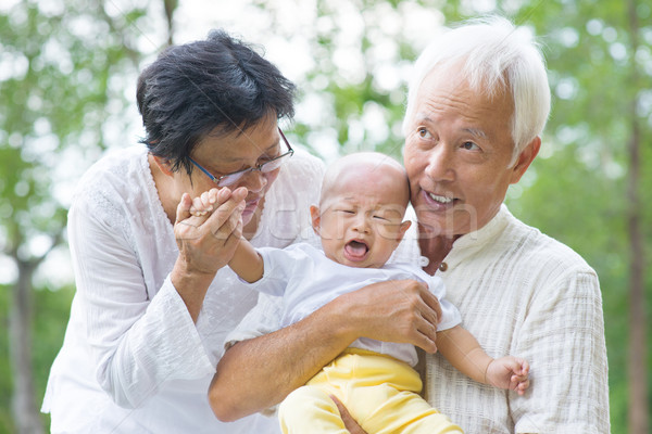 Asian crying baby comforted by grandparents at outdoor garden Stock photo © szefei