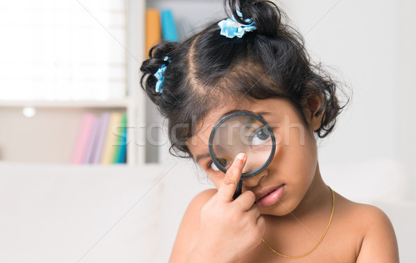 Indian girl peers at the camera through a magnifying glass Stock photo © szefei