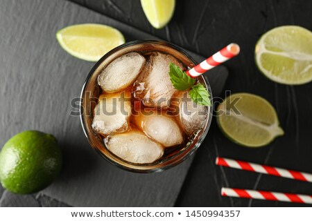 Foto stock: Glass With Ice Cola And Tubule On Black Background With Limes